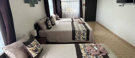 A hotel room with two beds, each with a patterned bedspread and pillows. There is a television mounted on the wall and a window with curtains.
