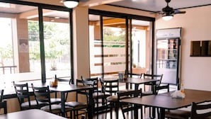 A restaurant interior with multiple tables and chairs, ceiling fans, and large windows allowing natural light. - Hotel del Rio (Liberia)