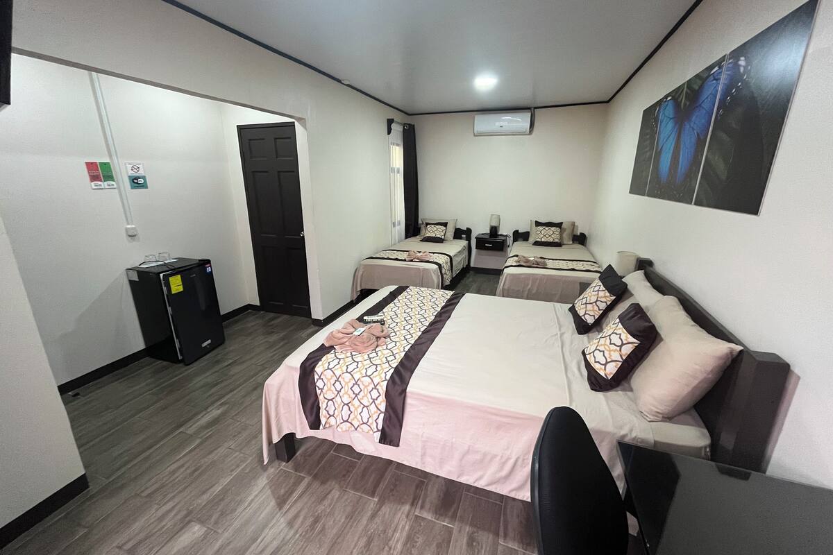 A hotel room with two beds, a desk, a chair, a wardrobe, and a small trash bin.