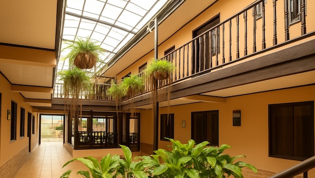A hotel lobby with a central atrium, a staircase, and hanging plants. - Hotel del Rio (Liberia)
