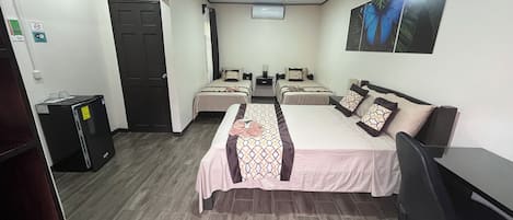 A hotel room with two beds, a desk, a chair, a refrigerator, and a door.