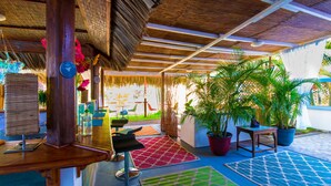 Un patio exterior con techo de paja, zonas de estar y plantas en macetas.