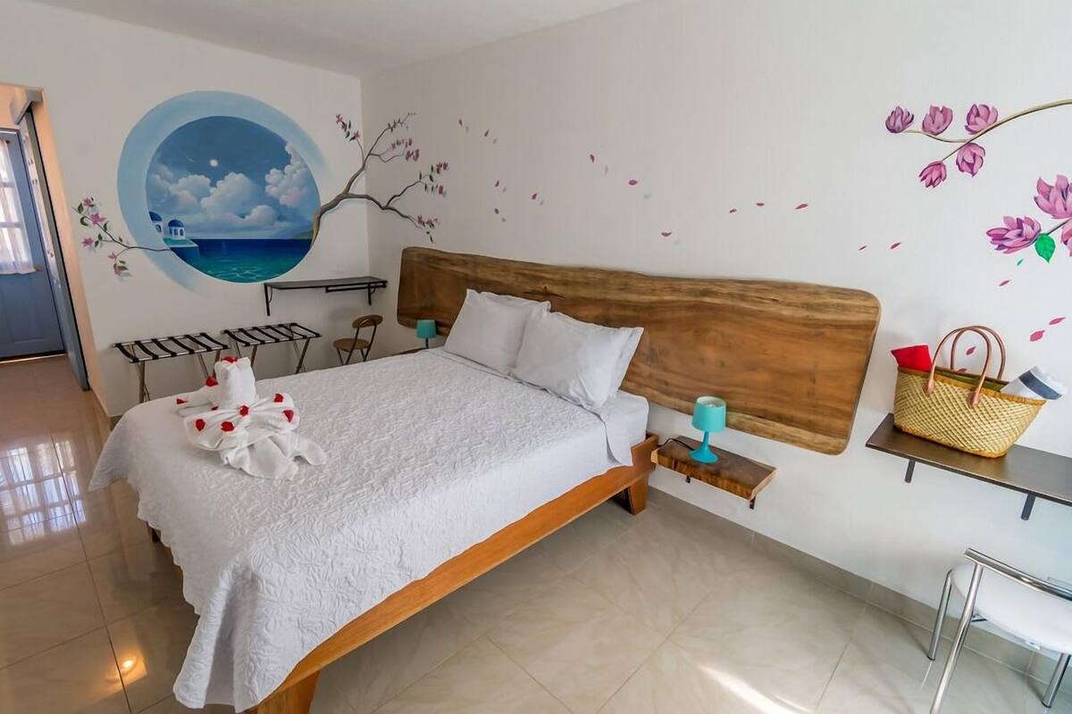 A neatly made bed with a white duvet, a wooden headboard, and a small bedside table with a lamp and a basket.