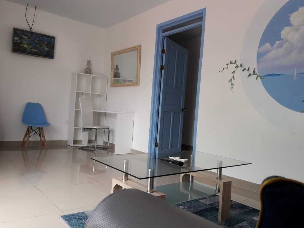 Een moderne woonkamer met een glazen salontafel, een blauwe stoel, een wit wandrek en een deur naar een andere kamer.