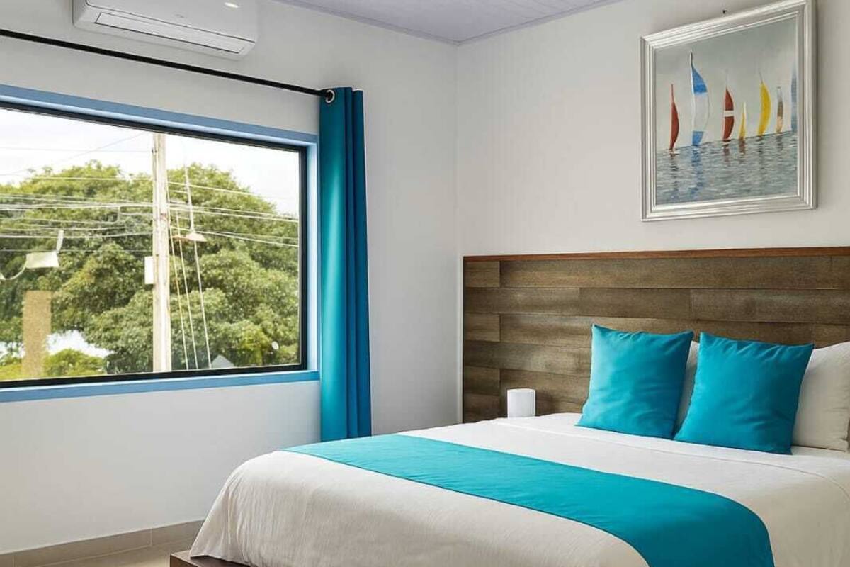 A modern hotel room with a large bed, a view of trees through the window, and a painting on the wall.