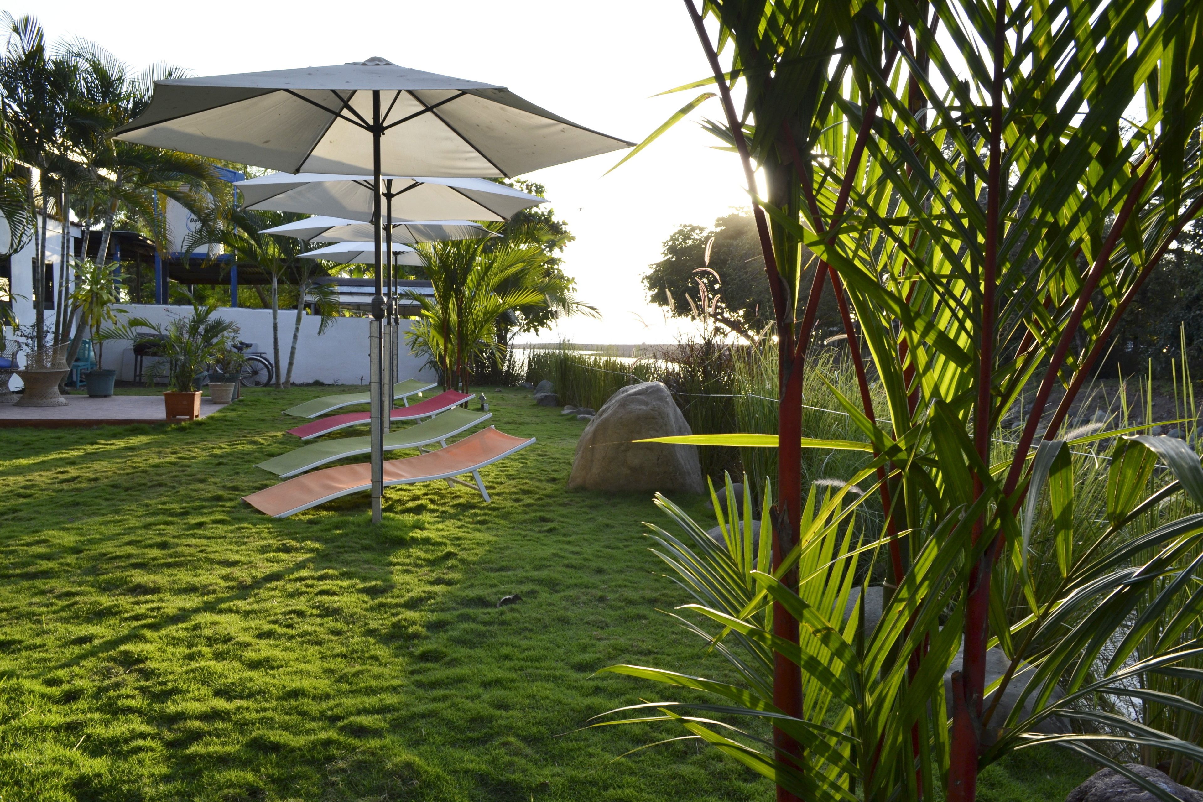 Un jardin bien entretenu, avec une pelouse verdoyante, un espace extérieur aménagé pour s’asseoir et de grands parasols qui offrent de l’ombre.