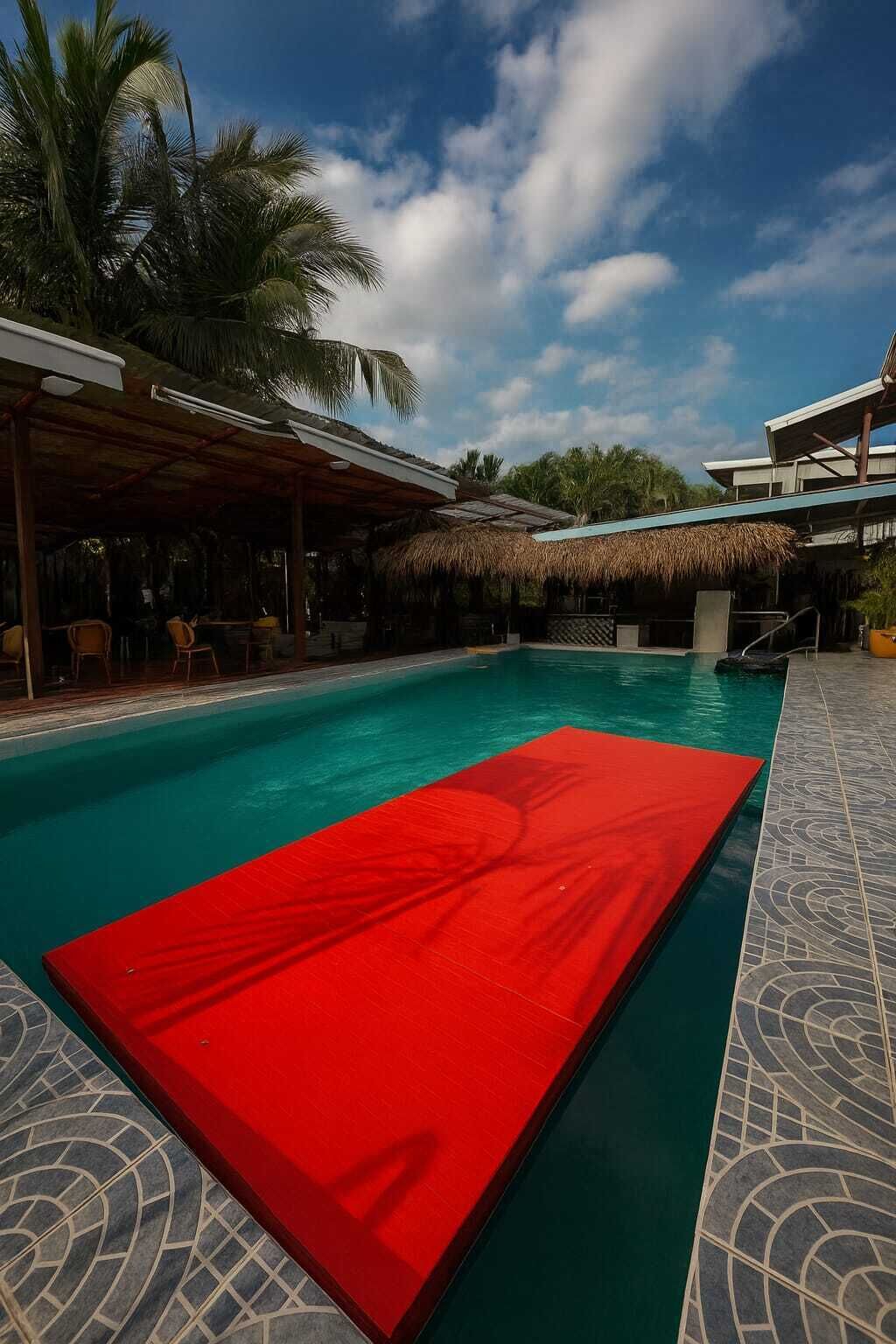 Ein Pool mit roher Liege, Palmen und einem überdachten Bereich mit Stühlen.