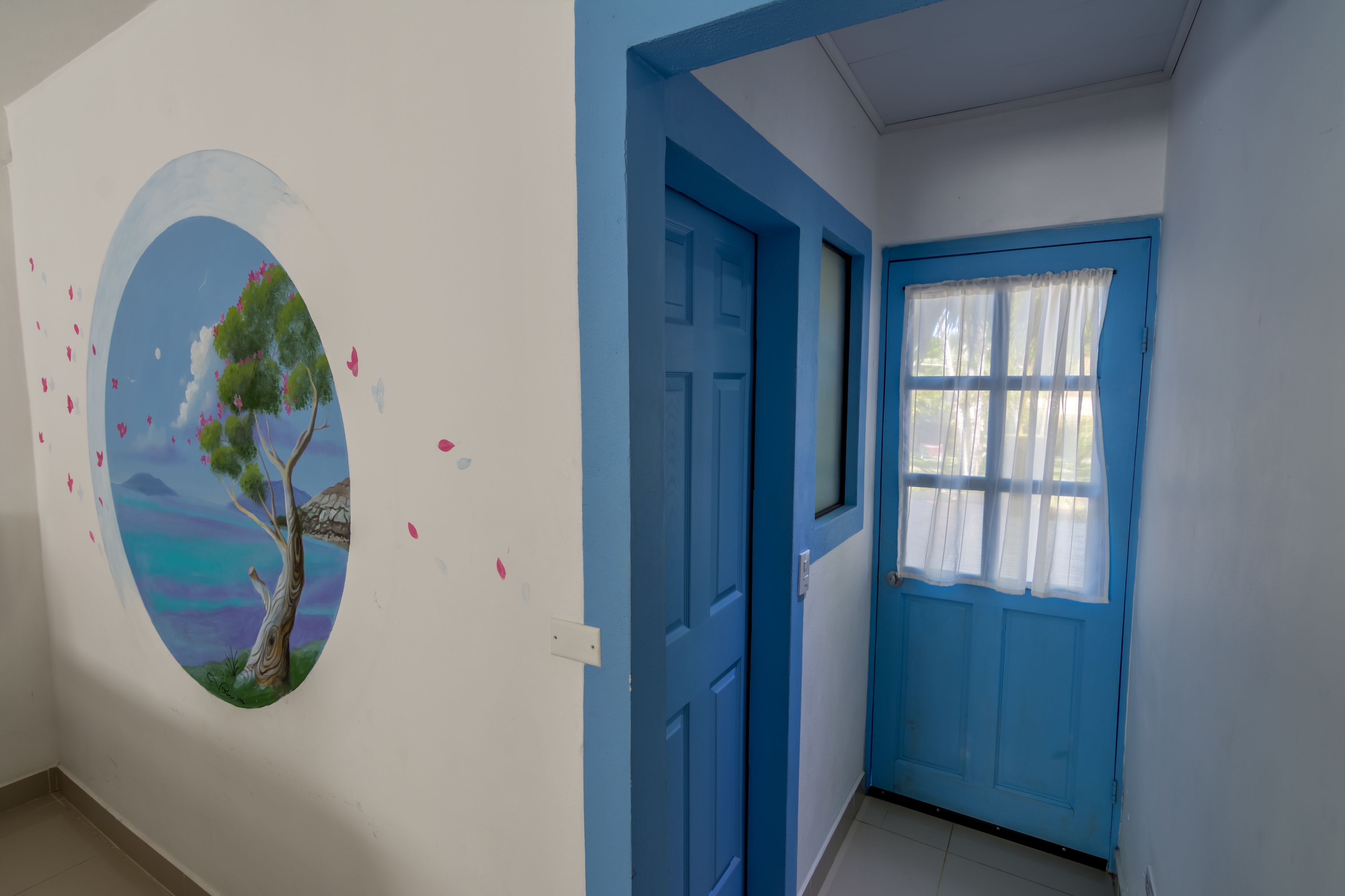 Passadís amb una porta blava i una finestra amb cortines blanques.