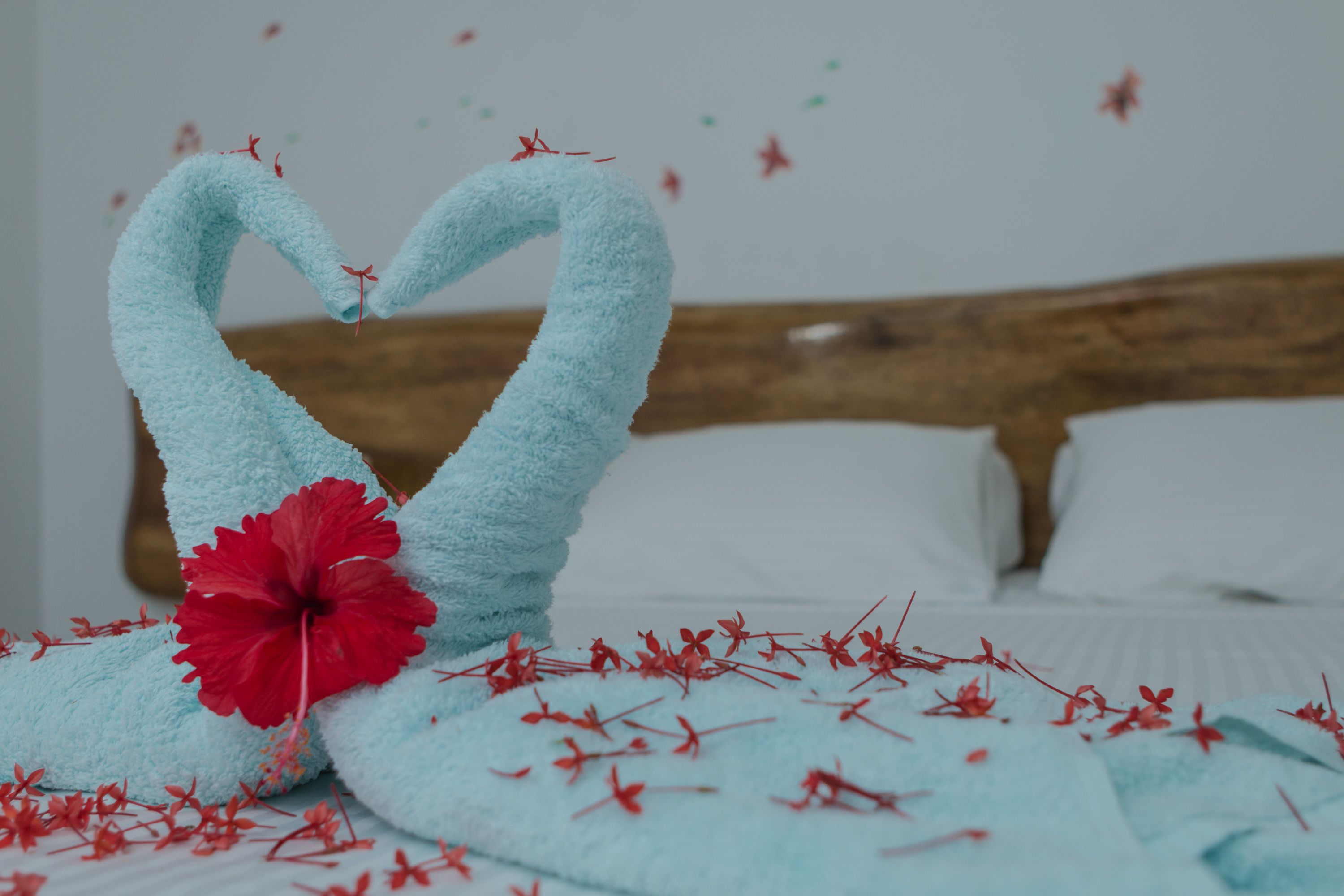 A bed with a wooden headboard, a blue towel, and red flowers.