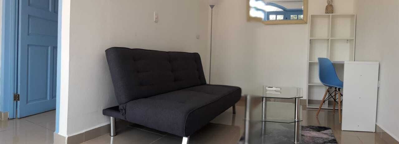 A room with a dark grey sofa, a small white table, a blue chair, and a white cabinet.