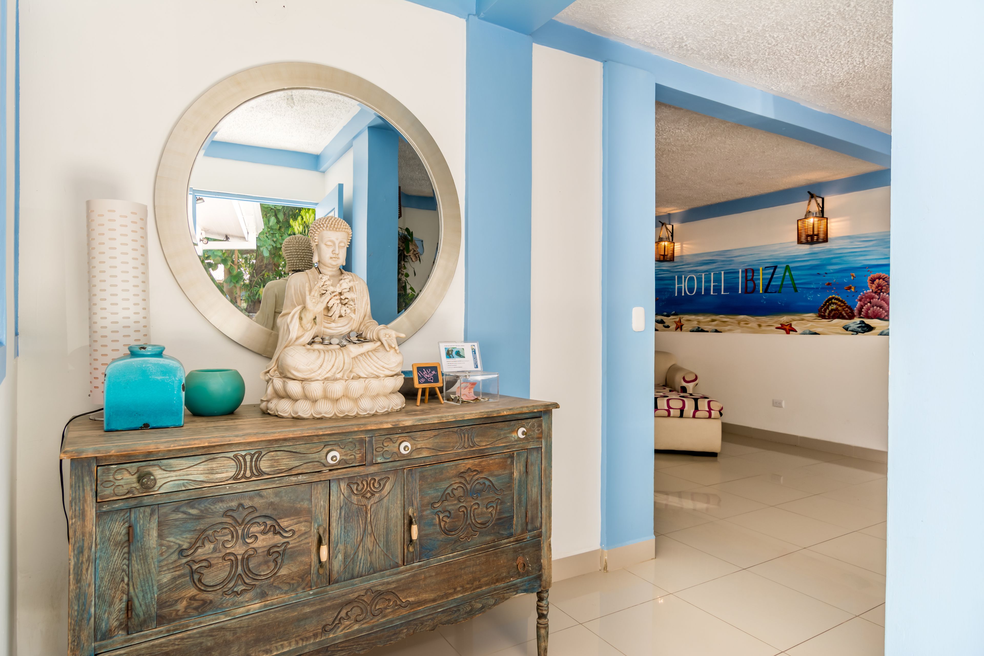 A room with a decorative wooden cabinet, a large round mirror, and a Buddha statue.