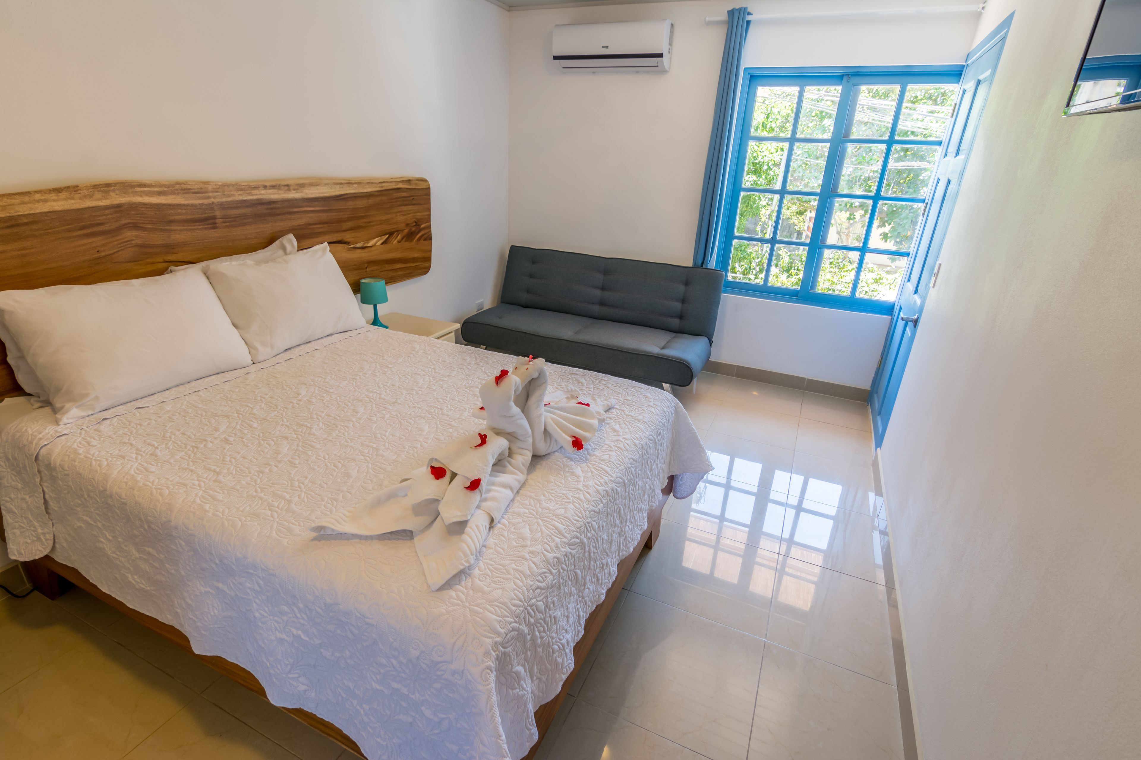A hotel room with a bed, a sofa, and a window with blue curtains.