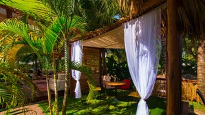 Un espacio de estar al aire libre cubierto con techo de paja, rodeado de palmeras y una valla de madera.