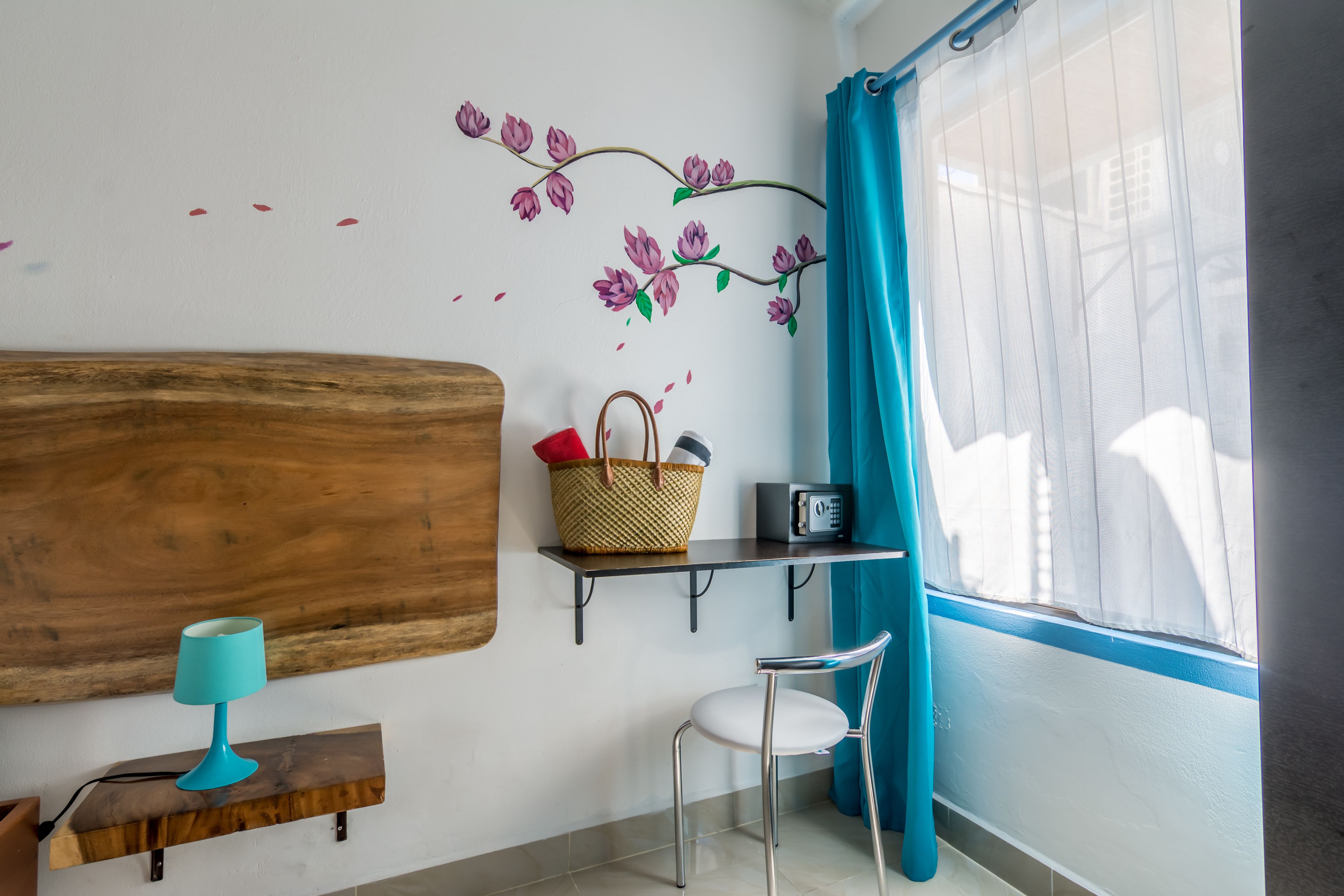 A room with a wooden headboard, a teal lamp, a basket with red items, a small shelf with a radio, and a chair.