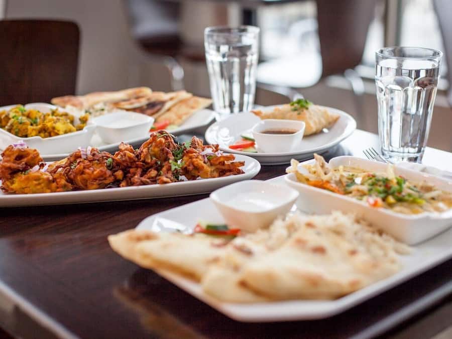 A table with various dishes, including fried items, flatbreads, and salads, accompanied by glasses of water.