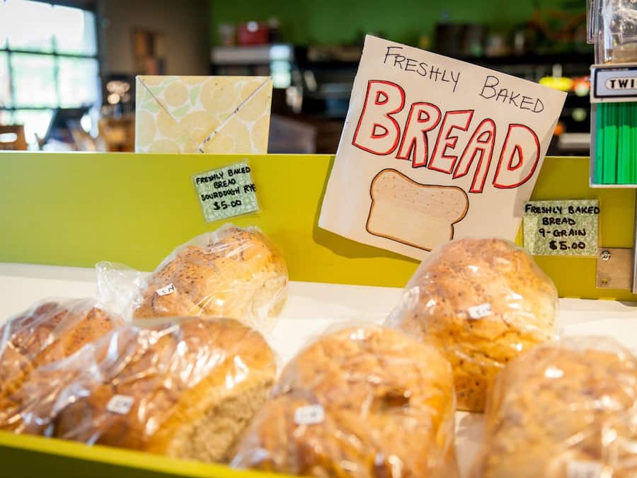 Una vitrina de panadería con varios tipos de pan, incluyendo un cartel que indica pan recién horneado a $5.00.