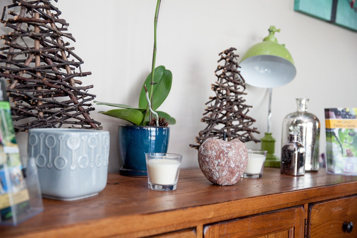 A wooden table with decorative items including a plant in a blue pot, a small candle, and a glass bottle.