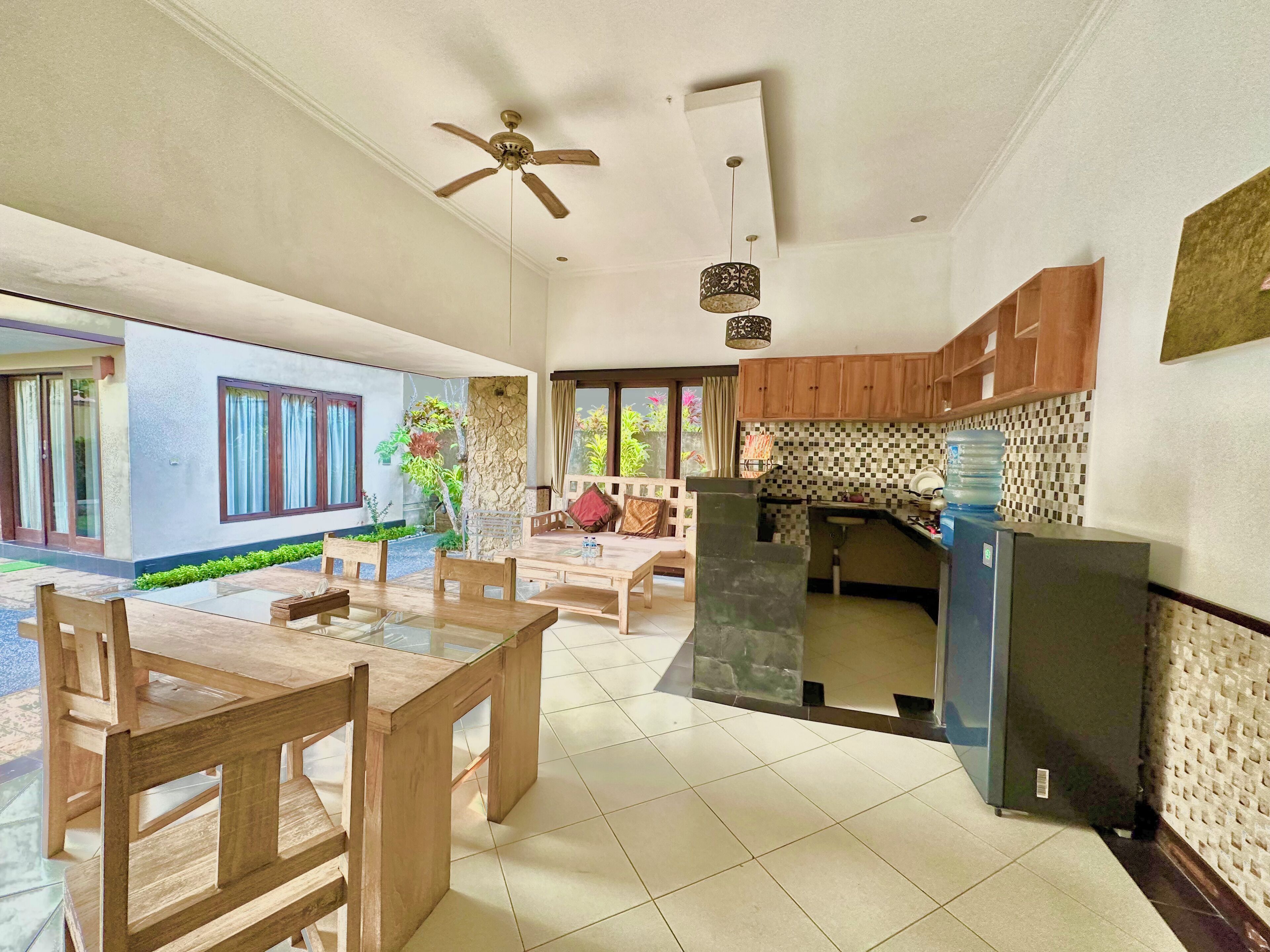 A spacious living area with a dining table, chairs, a sofa, and a kitchen area with wooden cabinets and a refrigerator.