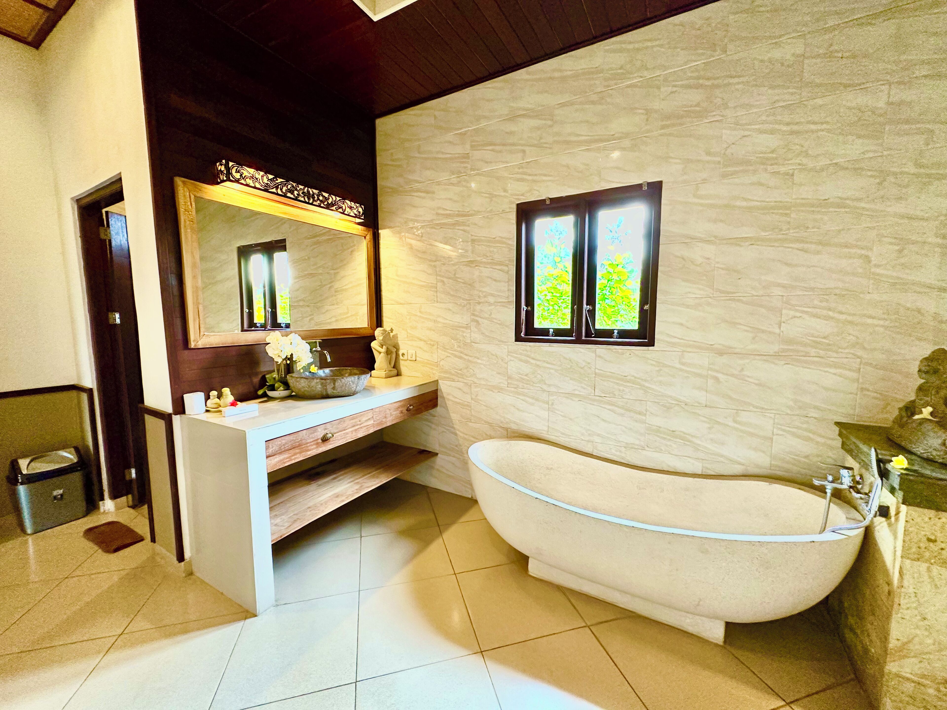 A bathroom with a freestanding bathtub, a vanity with a mirror, and a window with a view of greenery.