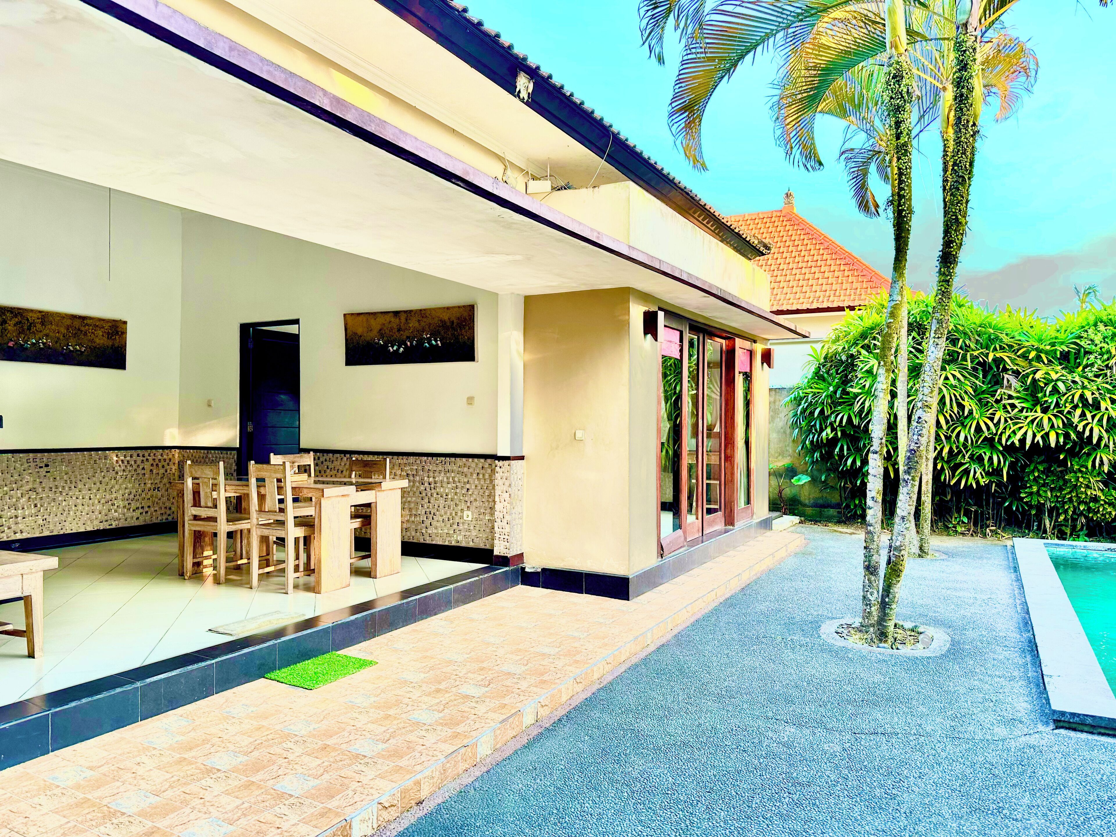 A covered outdoor area with a dining table and chairs, a tiled floor, and a pool.
