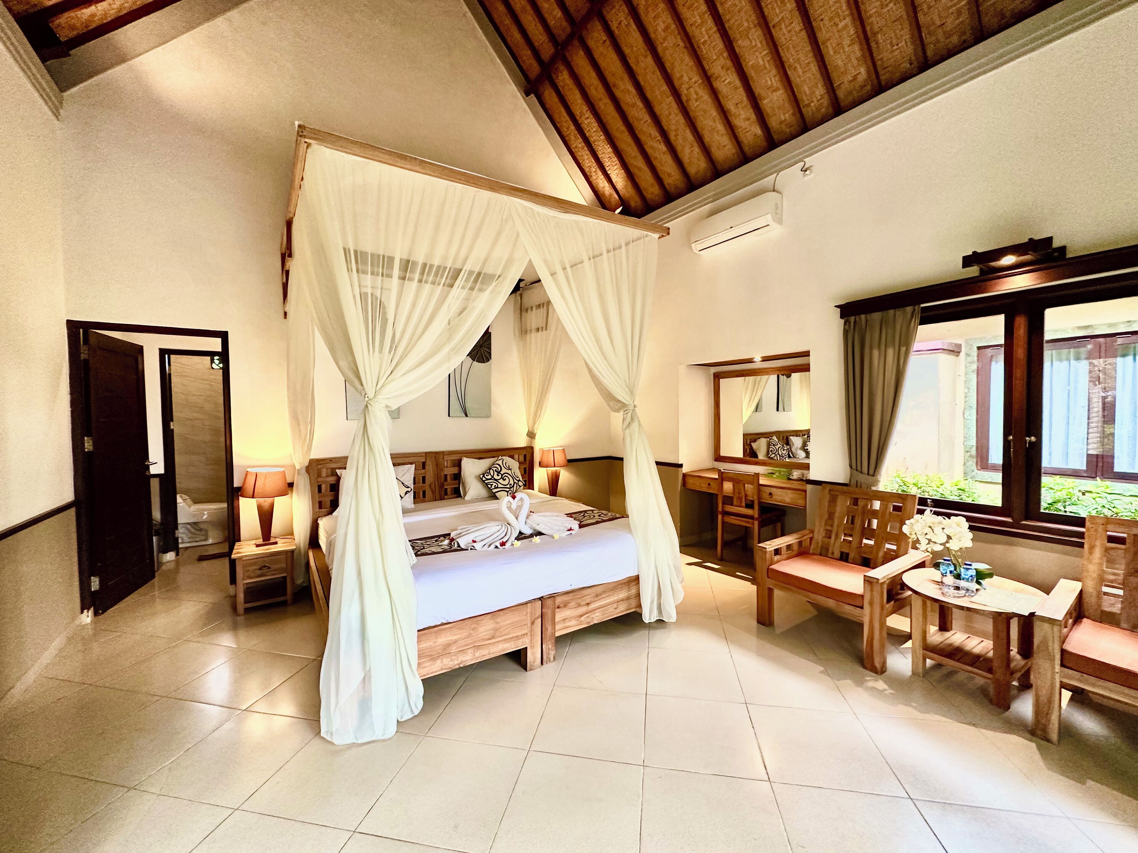 A spacious bedroom with a four-poster bed, a wooden desk, a chair, and a small table.