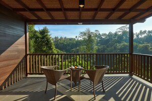 A balcony with wicker chairs and a table, overlooking a lush forest. - Jannata Resort and Spa (Ubud)