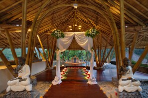A covered area with a central aisle, two Buddha statues, and a circular platform with a statue at the end. - Jannata Resort and Spa (Ubud)