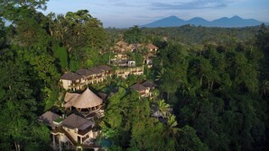 Un resort con varias construcciones tipo bungalow rodeado de bosque denso, que cuenta con un pabellón central y vistas a montañas lejanas.