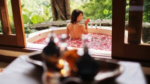 Una persona en una bañera llena de agua y pétalos de rosa, con vistas a la vegetación.