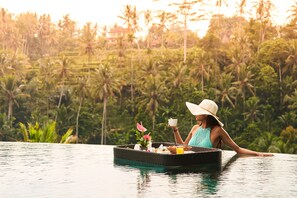 Una persona relajándose en una plataforma flotante en una piscina, con un paisaje tropical de fondo.