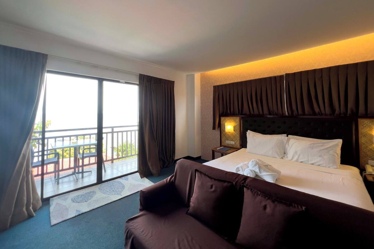 Una habitación de hotel con cama, sofá, mesita de noche y ventana con cortinas.