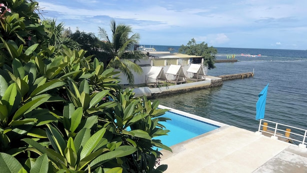 A pool area with a view of the sea, surrounded by lush greenery. - Aozora Seaside Mactan (Lapu-Lapu)