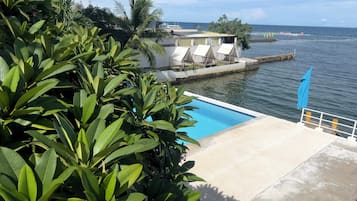 A pool area with a view of the sea, surrounded by lush greenery.