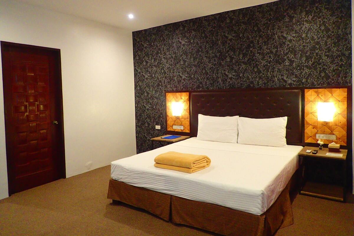 Habitación de hotel con una cama grande, dos mesitas de noche, un cabecero de madera y un papel tapiz estampado.