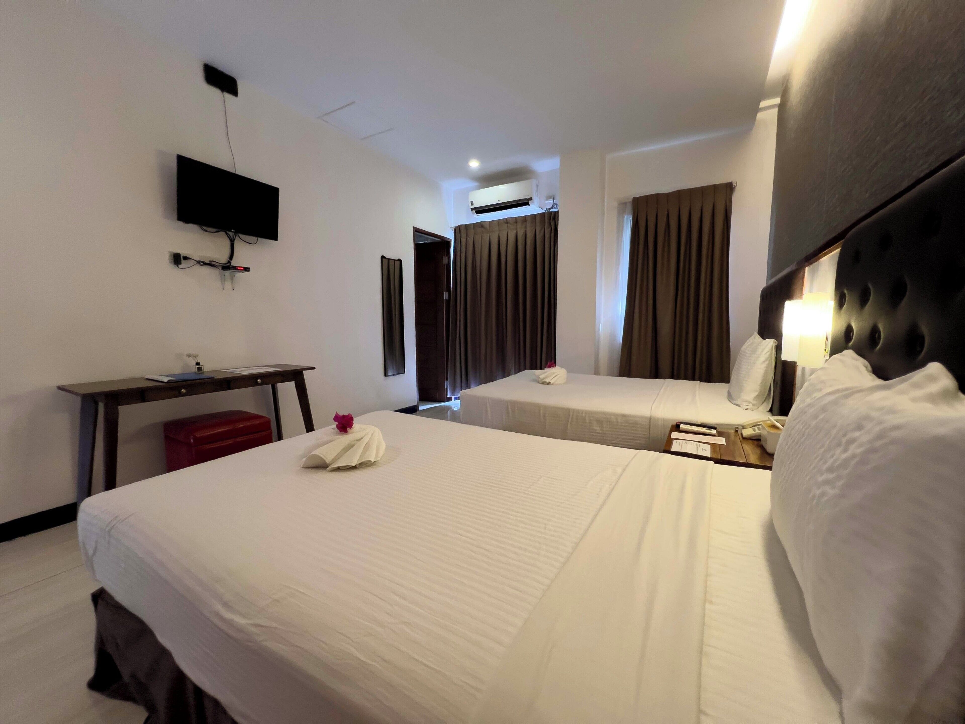 Une chambre d’hôtel avec deux lits, un bureau, un téléviseur à écran plat et un appareil de climatisation.