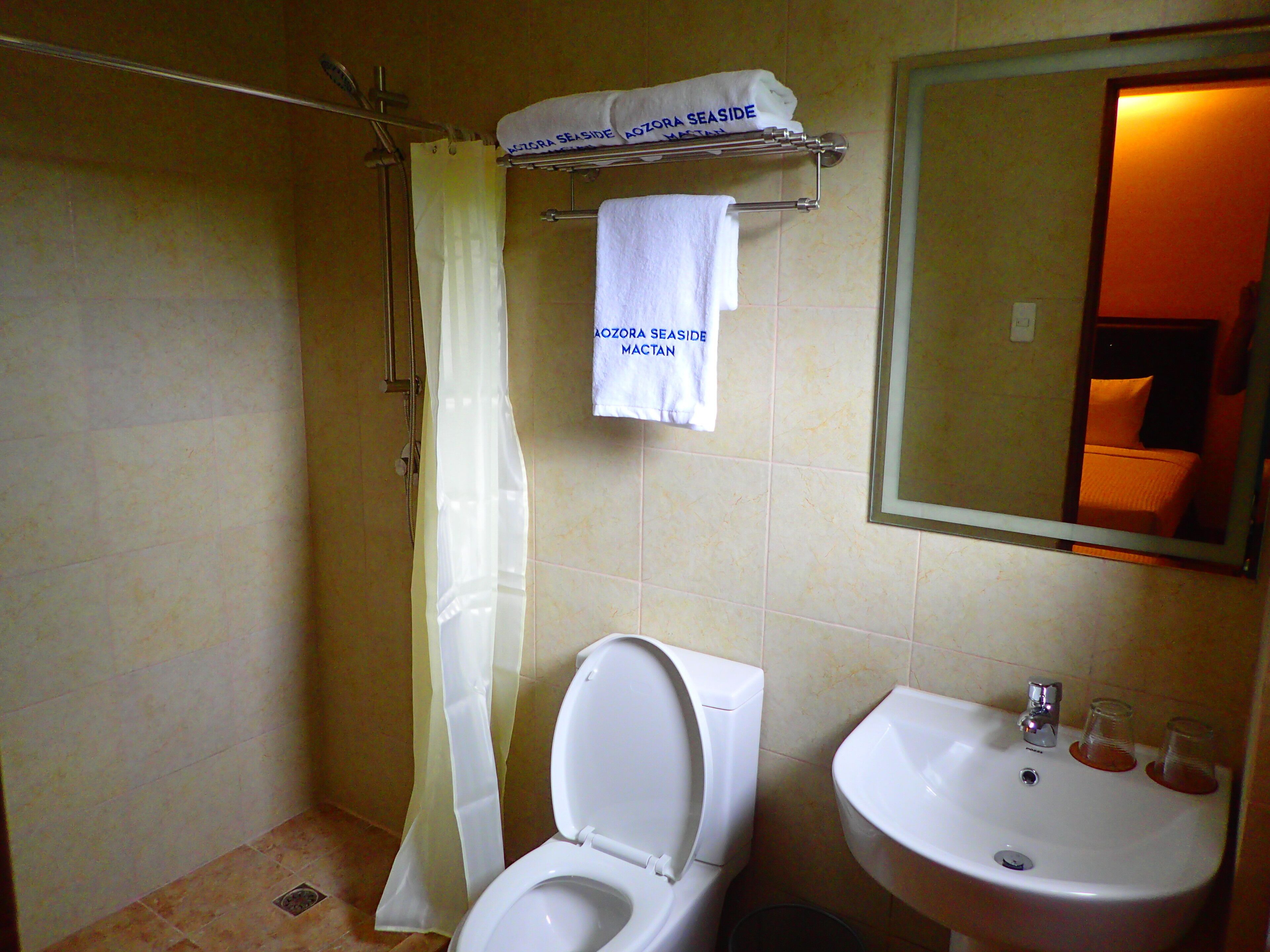 A bathroom with a toilet, sink, and shower curtain. There are towels hanging on a rack above the toilet.