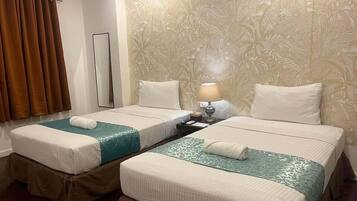 A hotel room with two beds, a nightstand, a lamp, and a curtain.
