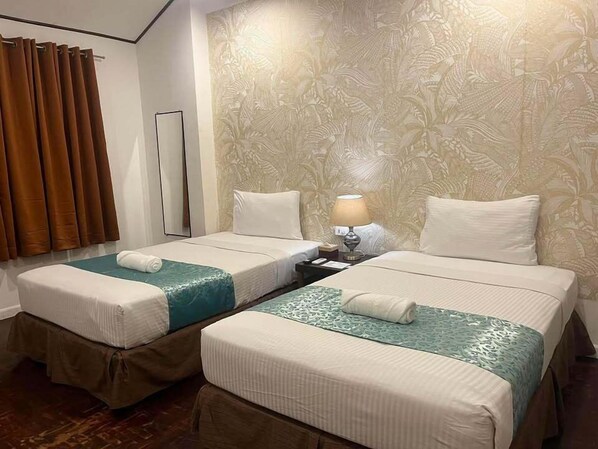 A hotel room with two beds, a nightstand, a lamp, and a curtain.