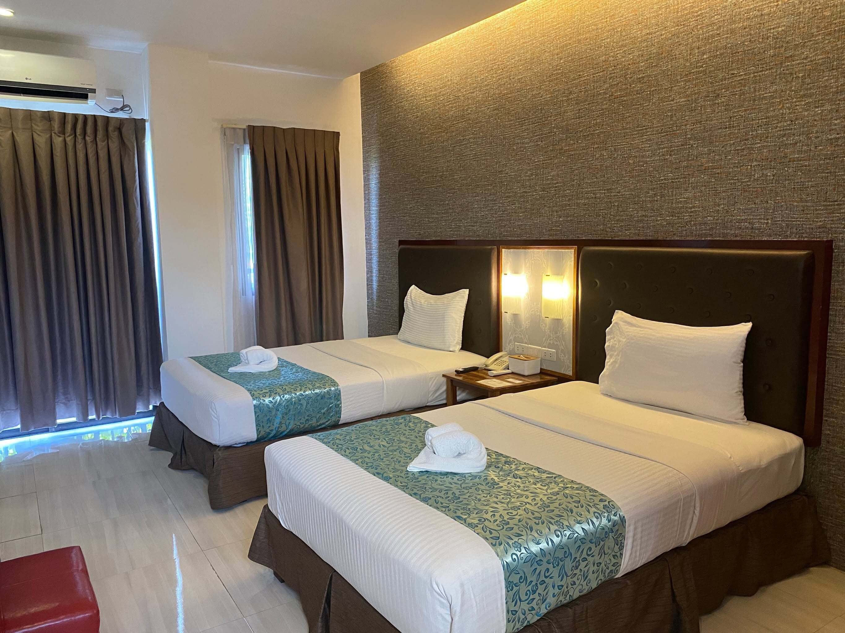 A hotel room with two beds, a nightstand, a telephone, and a wall-mounted light fixture.