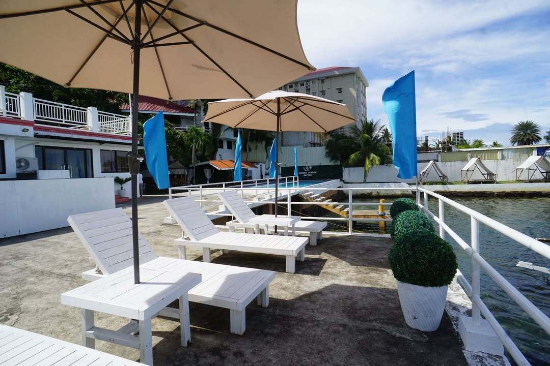 Un espace de détente aménagé sur le toit, avec des chaises longues blanches et un grand parasol, offrant une vue sur une étendue d’eau.