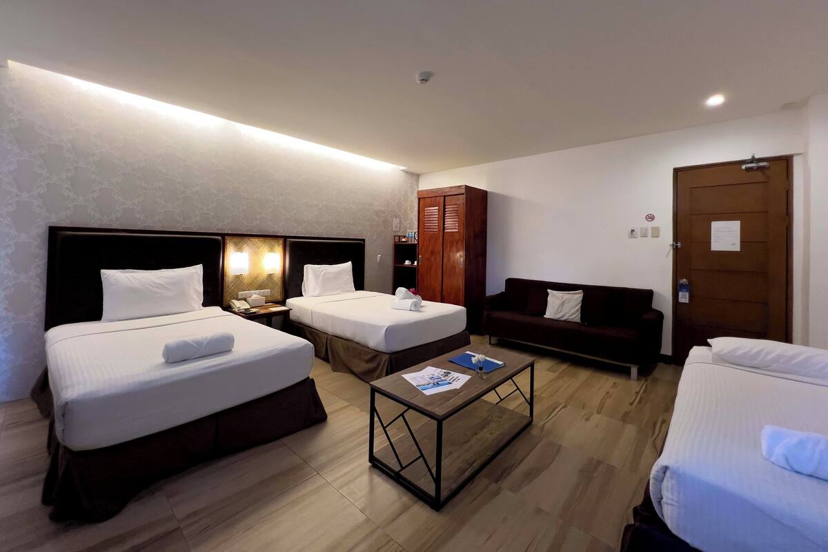 Habitación de hotel con dos camas, un sofá, un armario de madera, una mesa de centro y una puerta con un cartel.