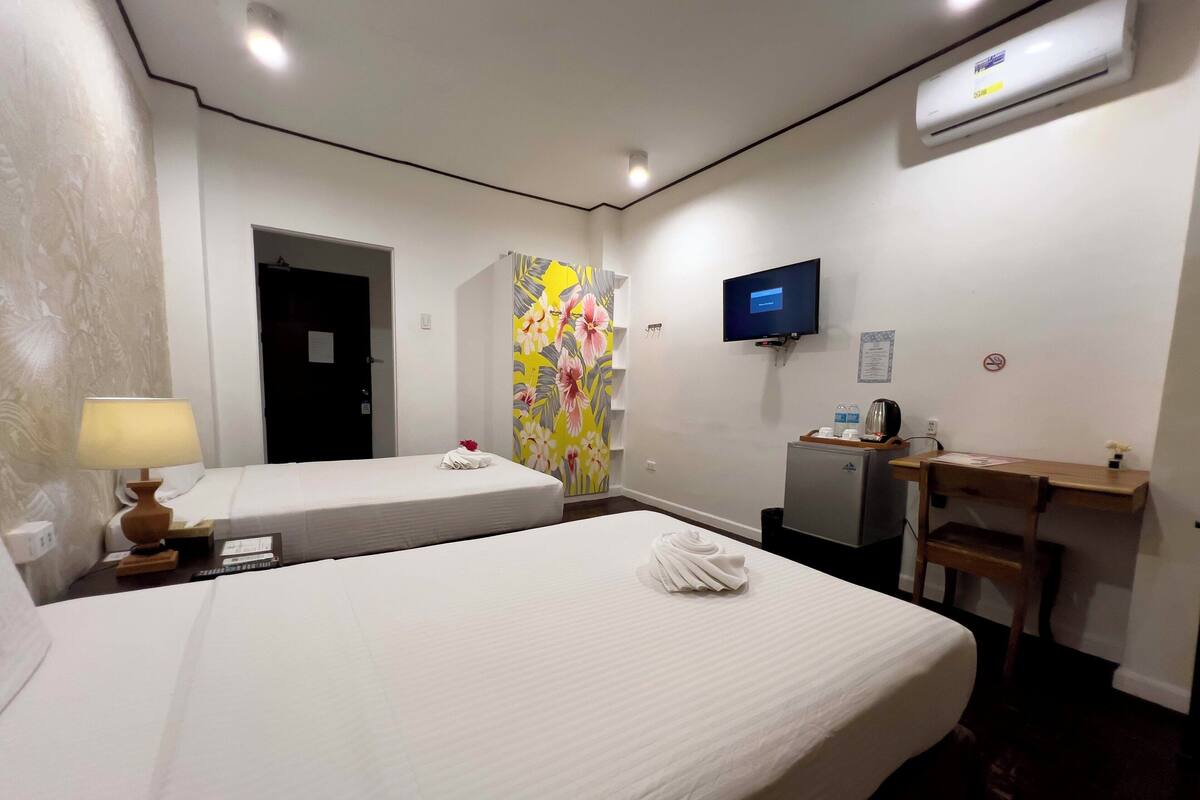 Habitación de hotel con dos camas, un escritorio, un televisor y un refrigerador pequeño.