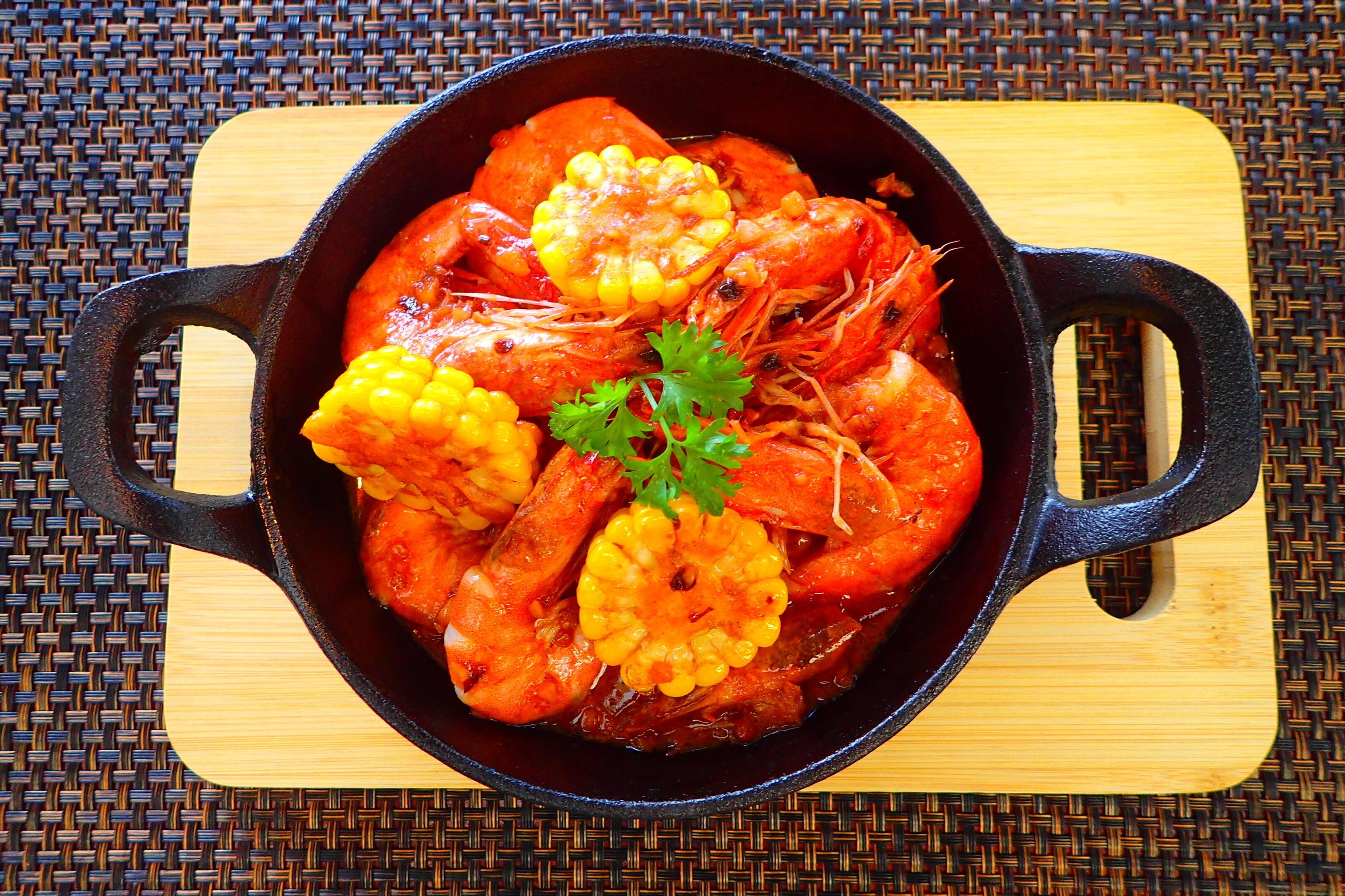 A black cast iron skillet with shrimp and corn on a wooden board.