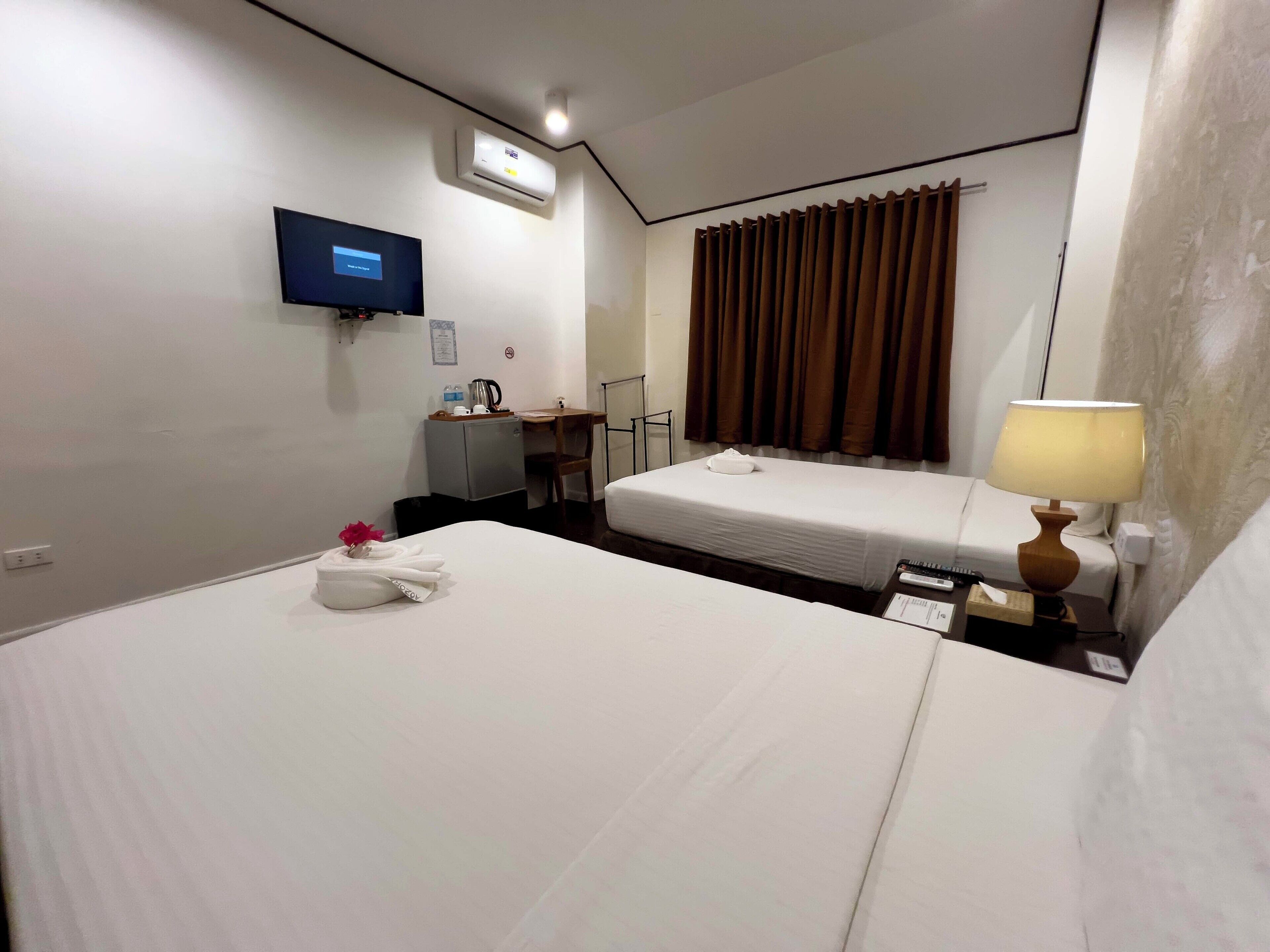 A hotel room with two beds, a desk, a television, an air conditioner, and a window with curtains.
