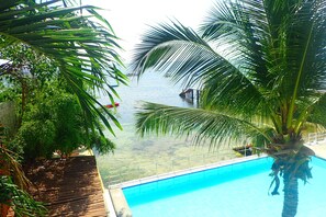 A pool with clear water, surrounded by palm trees and a view of the sea. - Aozora Seaside Mactan (Lapu-Lapu)