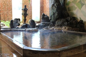 A hot spring area with a stone fountain, rocky formations, and a tiled floor. - Marumo (Tottori)