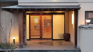 A traditional Japanese entrance with a wooden gate, a potted plant, and a lamp. - Marumo (Tottori)