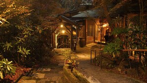A traditional Japanese building with a wooden structure, surrounded by lush greenery and stone pathways. - Oyado Hanabou (Minamioguni)