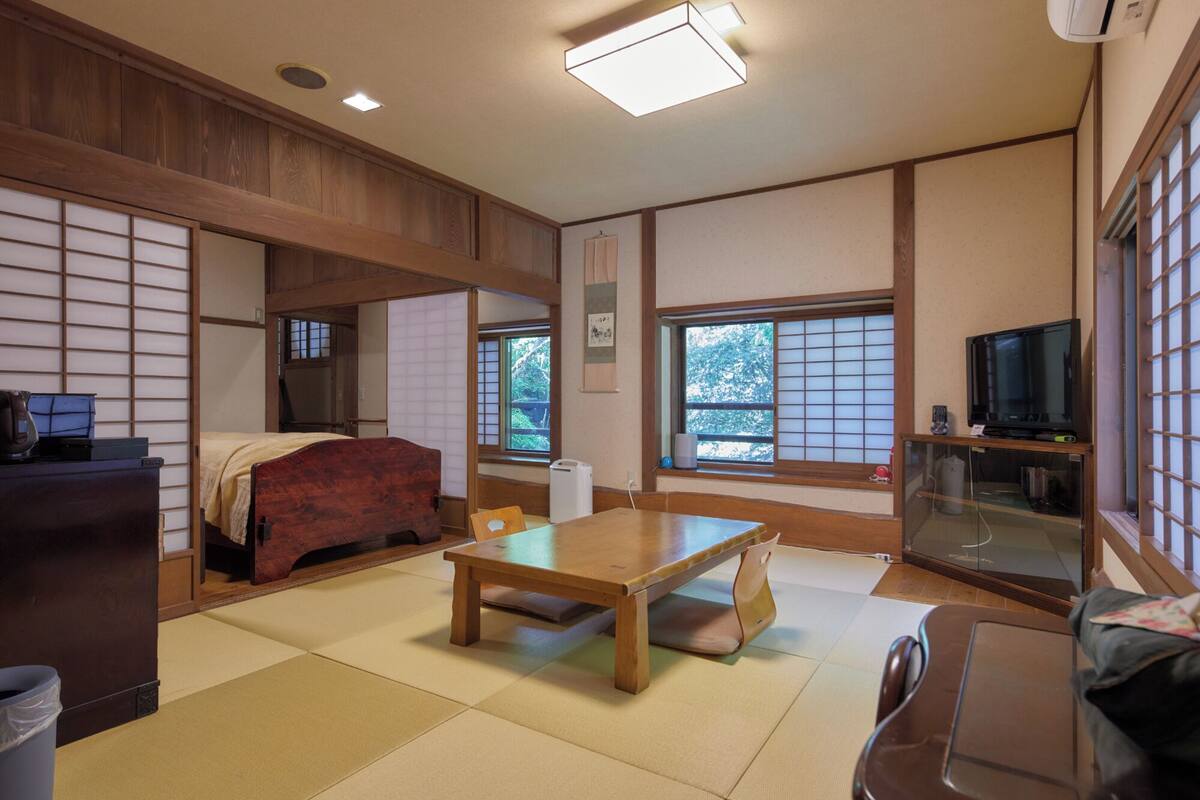 Une pièce de style japonais traditionnel, avec un sol recouvert de tatamis, une basse table en bois, un canapé, un téléviseur et des portes coulissantes.