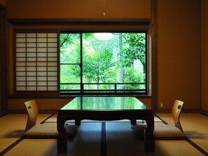 A tatami mat room with a low table and two cushions, a shoji screen, and a view of greenery outside. - Oyado Hanabou (Minamioguni)